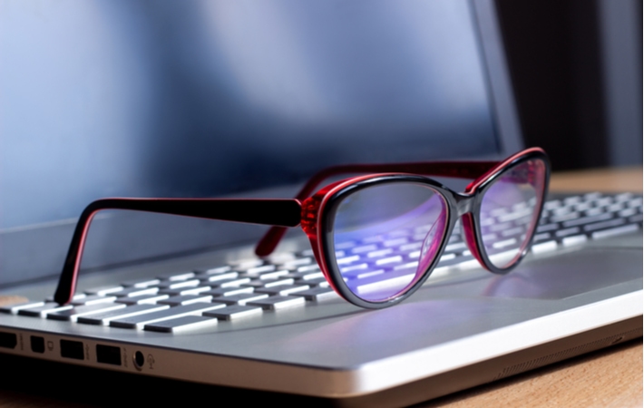 A pair of blue light glasses resting on the keyboard of a laptop