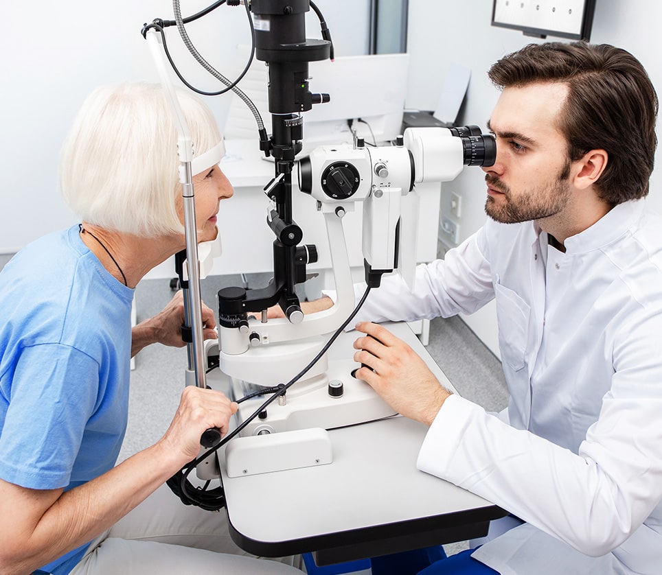 A male optometrist examines an older female patient's eyes for any conditions related to diabetes.