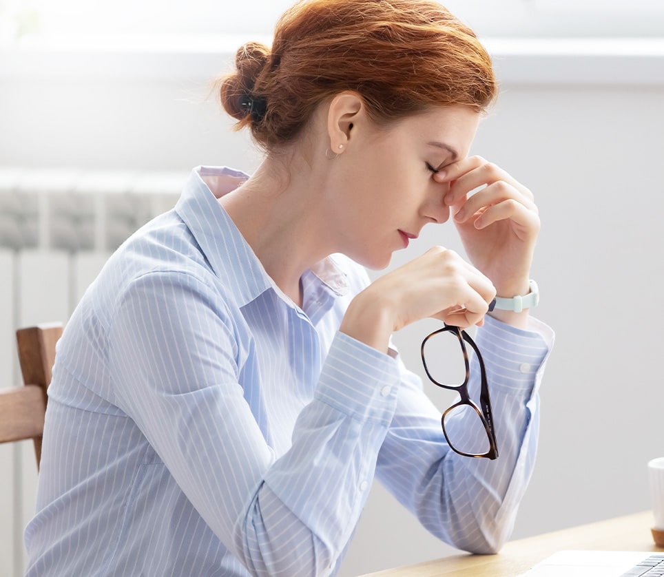 A woman taking off her glasses and rubbing her eyes due to digital eye strain.