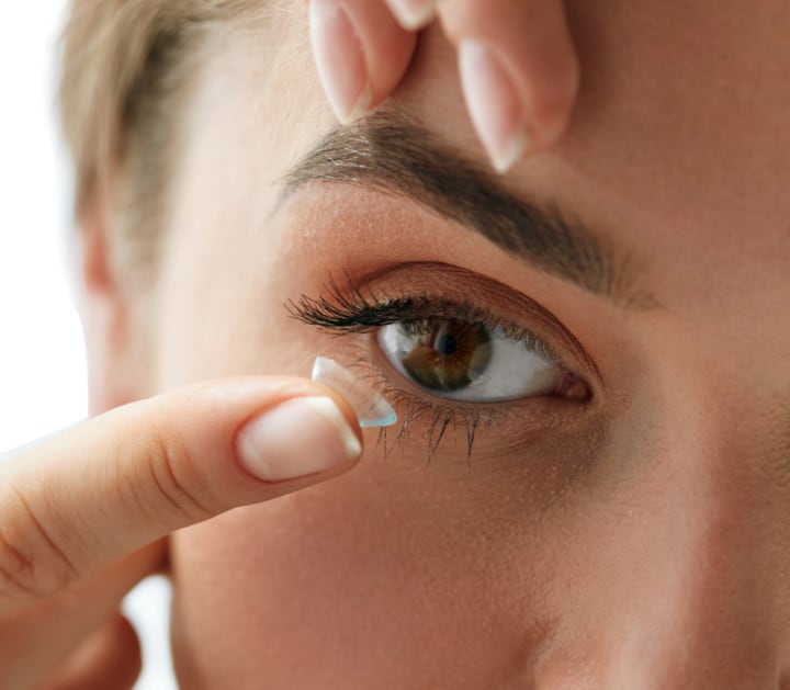 women inserting a contact lens into her eye